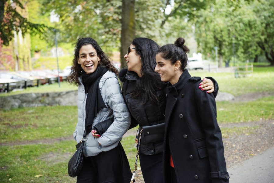 Three young women walking together in a park. They are laughing and seems to be good friends.