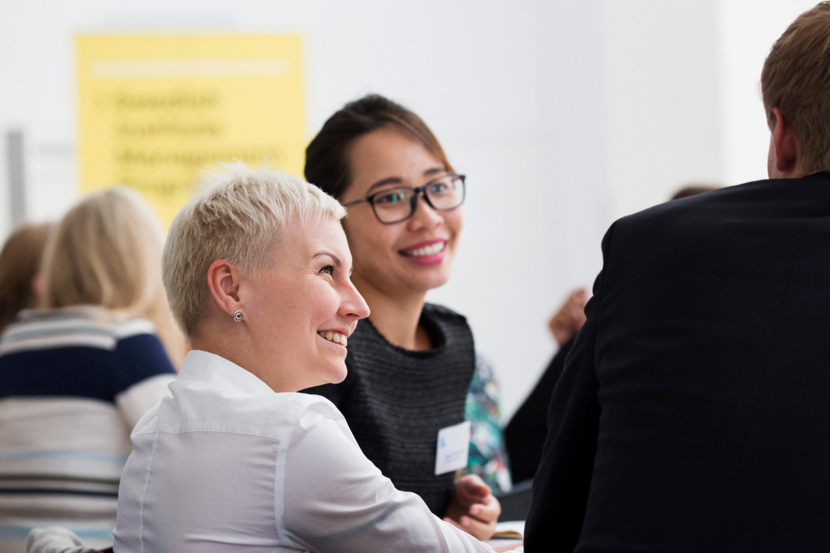 Two smiling conference participants talking to person outside of picture