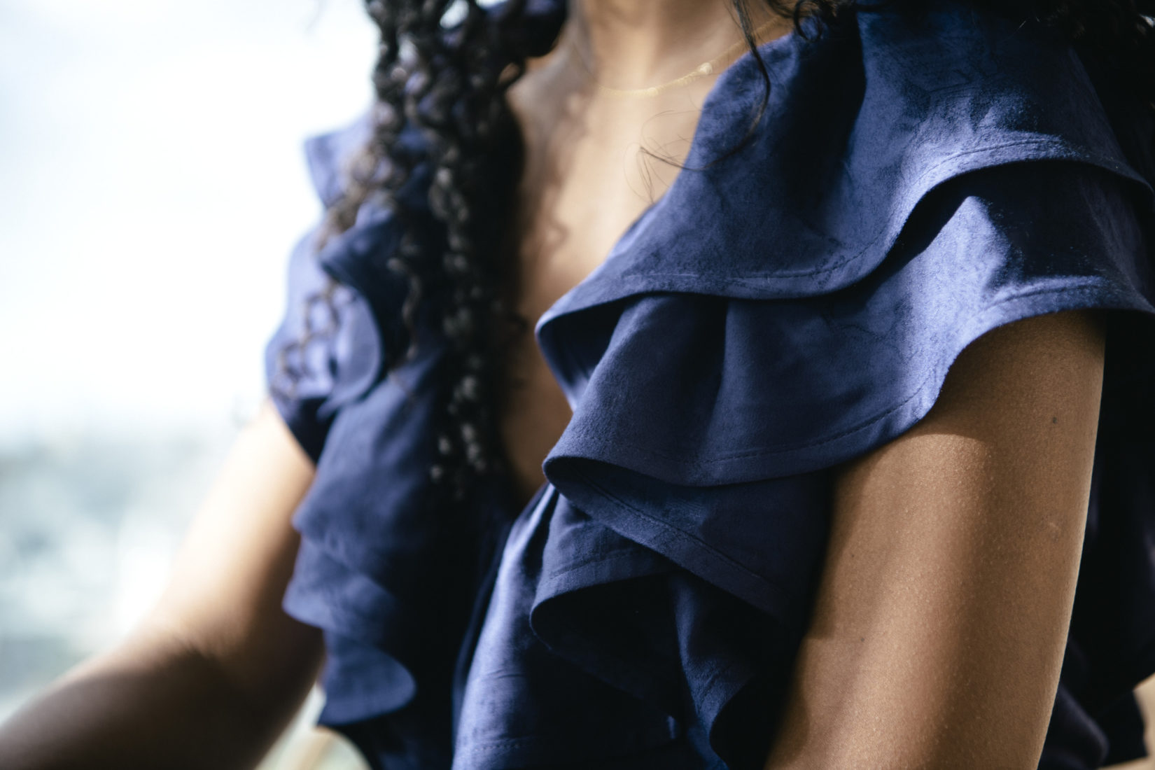 A close-up on a model with the neckline draping of a sleeveless blue dress in focus. Photographer: Margareta Bloom