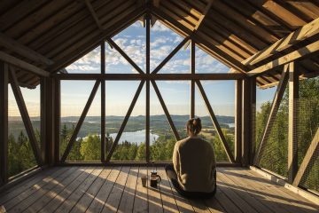 Person sitting in a wooden loft house looking out at a scenic view.