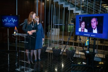 Ambassadör Annika Ben David och översättaren Marijana Maksimovic står på en scen och samtalar med Dina och Jovan Rajs, som syns på en bildskärm bredvid dem.