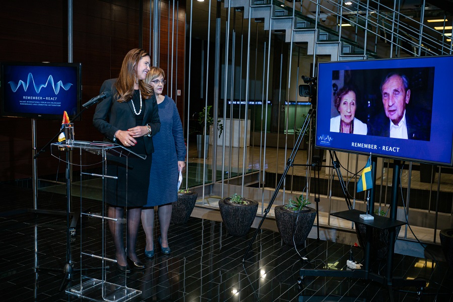 Ambassadör Annika Ben David och översättaren Marijana Maksimovic står på en scen och samtalar med Dina och Jovan Rajs, som syns på en bildskärm bredvid dem.
