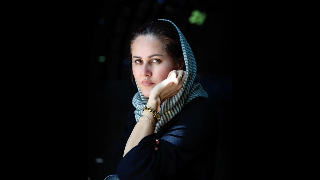 Färgfotografi av Sahraa Karimi som stödjer hakan i handen och tittar in i kameran.