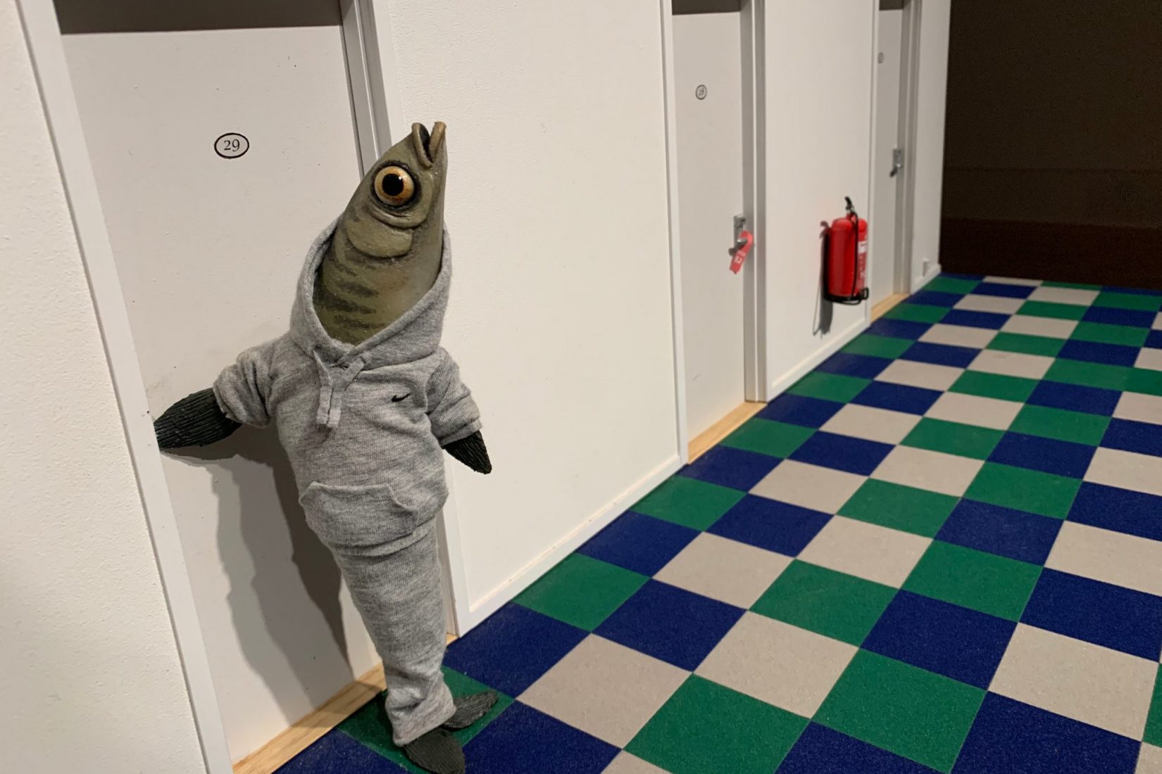 Bilden kommer från den animerade filmen The Burden och föreställer en grön fisk i grå träningskläder som är på väg in i ett hotellrum.