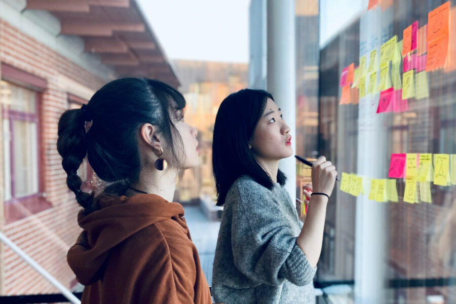 Två kvinnor står framför en glasvägg täckt med post-it-lappar