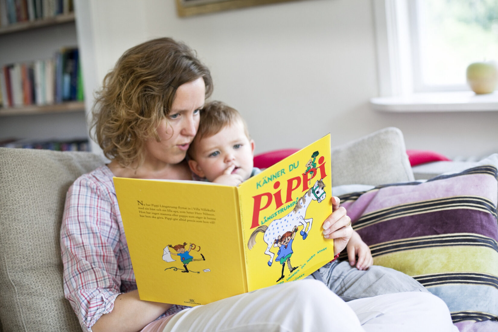 En kvinna har ett barn i knät. De läser en bok om Pippi Långstrump tillsammans.