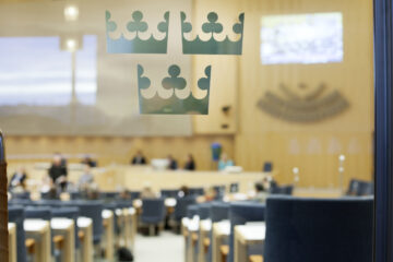 Riksdagssalen sedd genom en glasdörr med symbolen "tre kronor".
