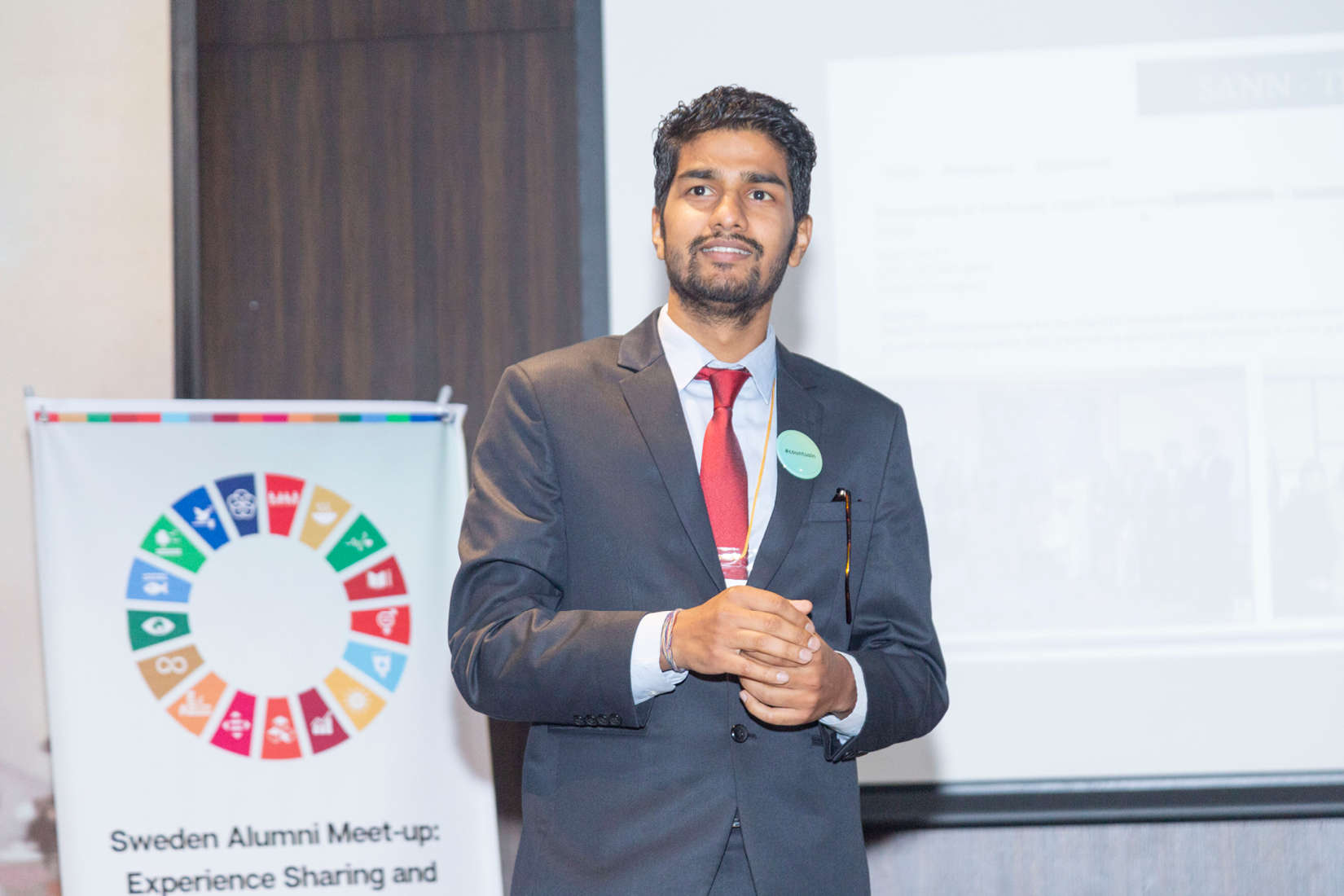 Raj standing in front of an illustration of the UN Sustainable Development Goals.