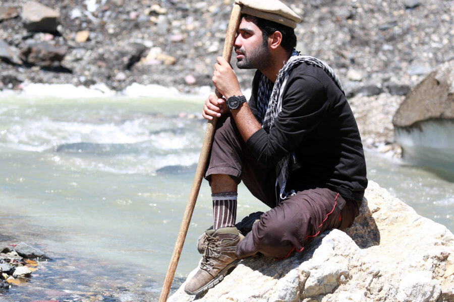 A man sitting on a cliff in a river holding a stick.