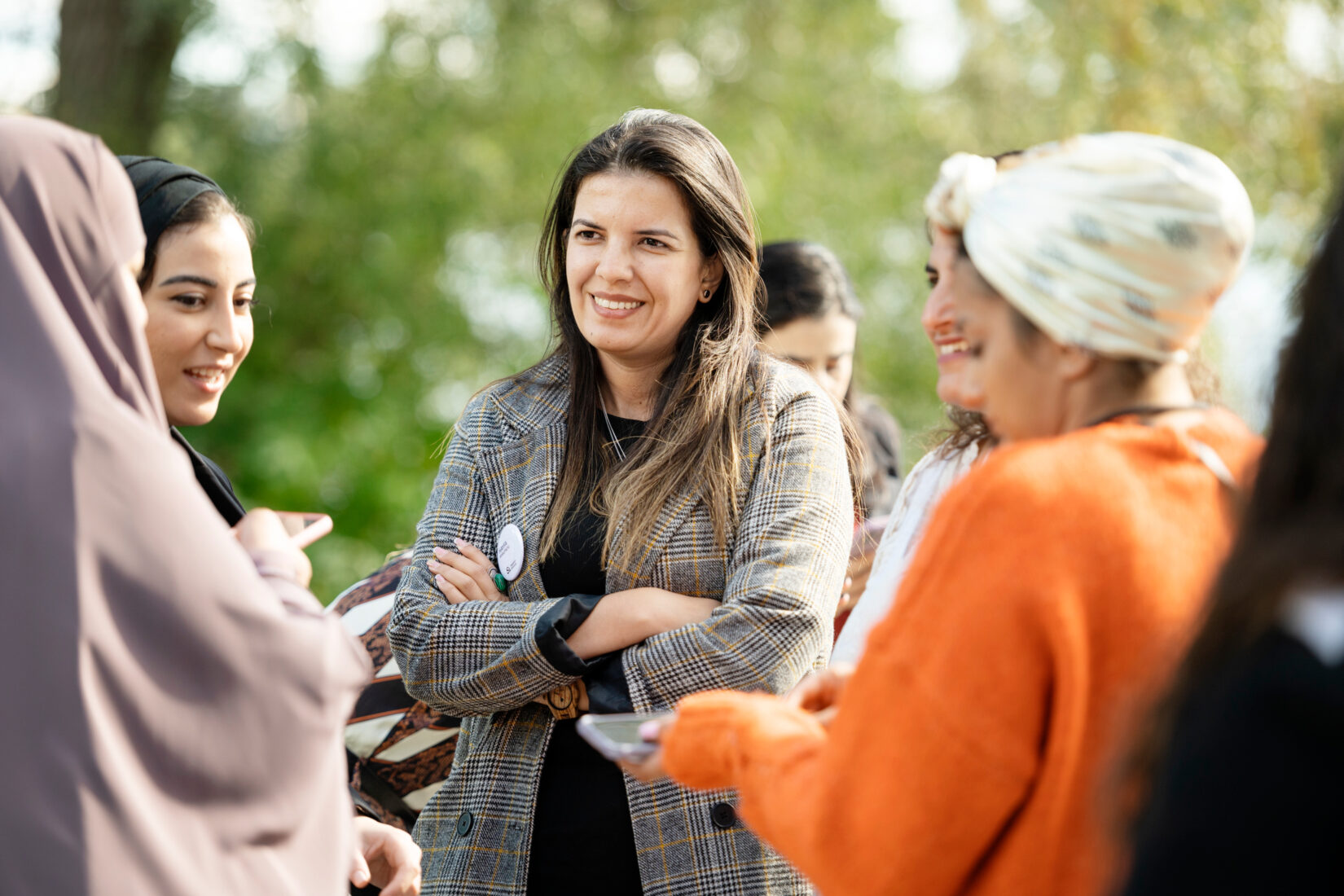A group of women is standing outside in the sun and having a discussion. They look happy and connected.