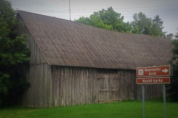 Grå träbyggnad och vägskylt där det står Nuckö kyrka