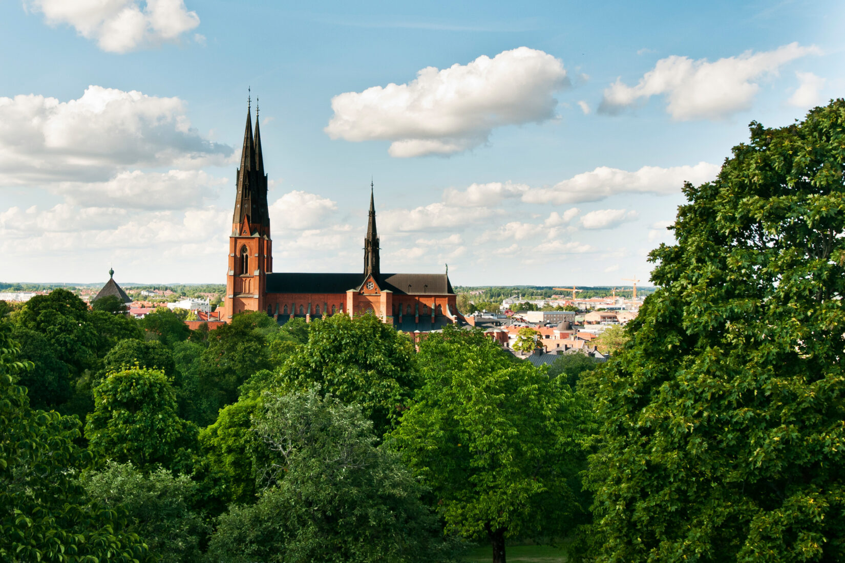 Uppsala domkyrka med gröna träd framför och blå himmel