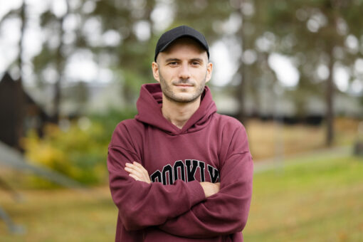 Man in red sweater and cap, crossing his arms.