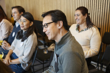 2 men and 2 women smiling while listening to someone speak