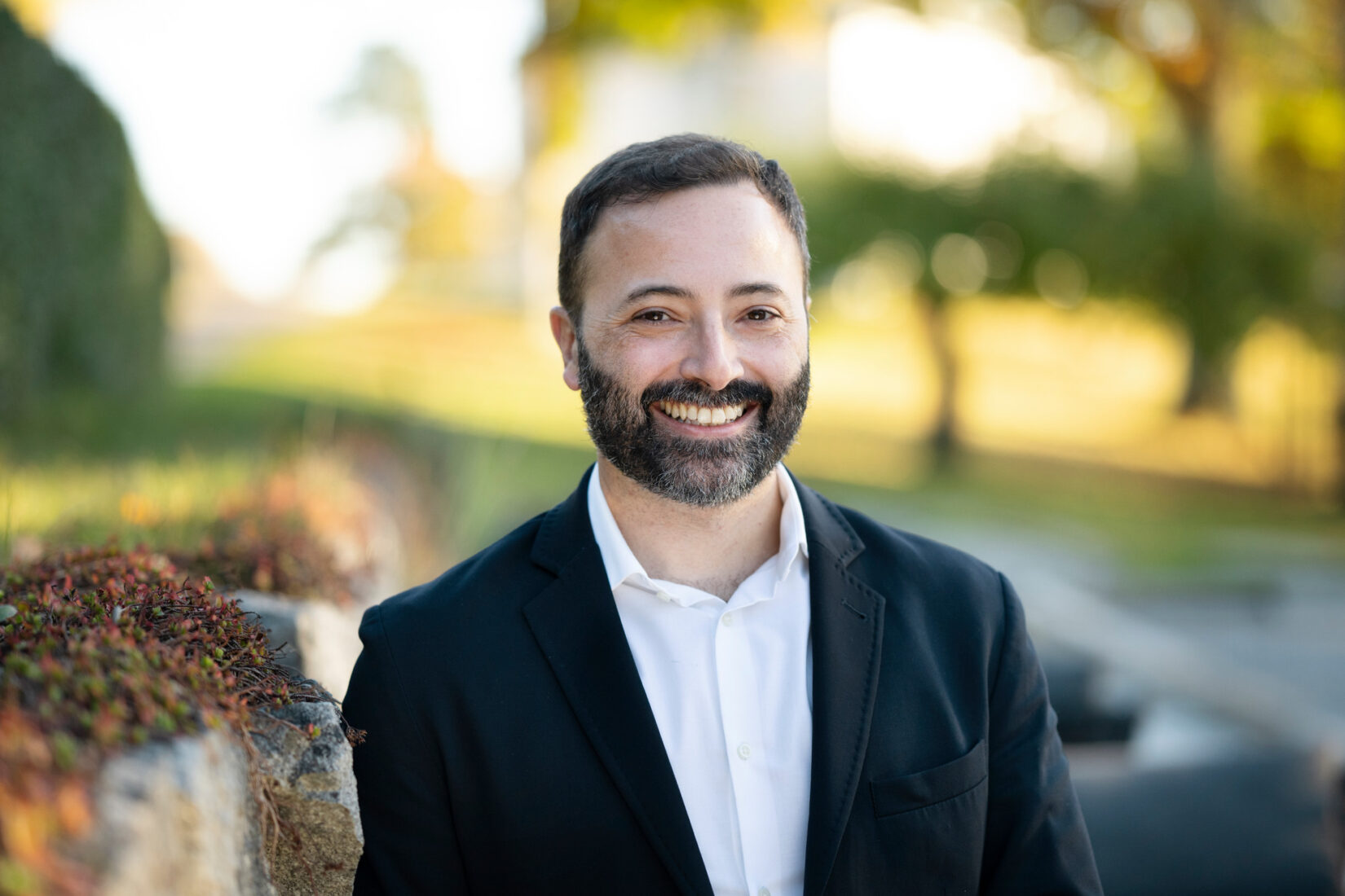 Man in beard, shirt and jacket smiling to the camera.