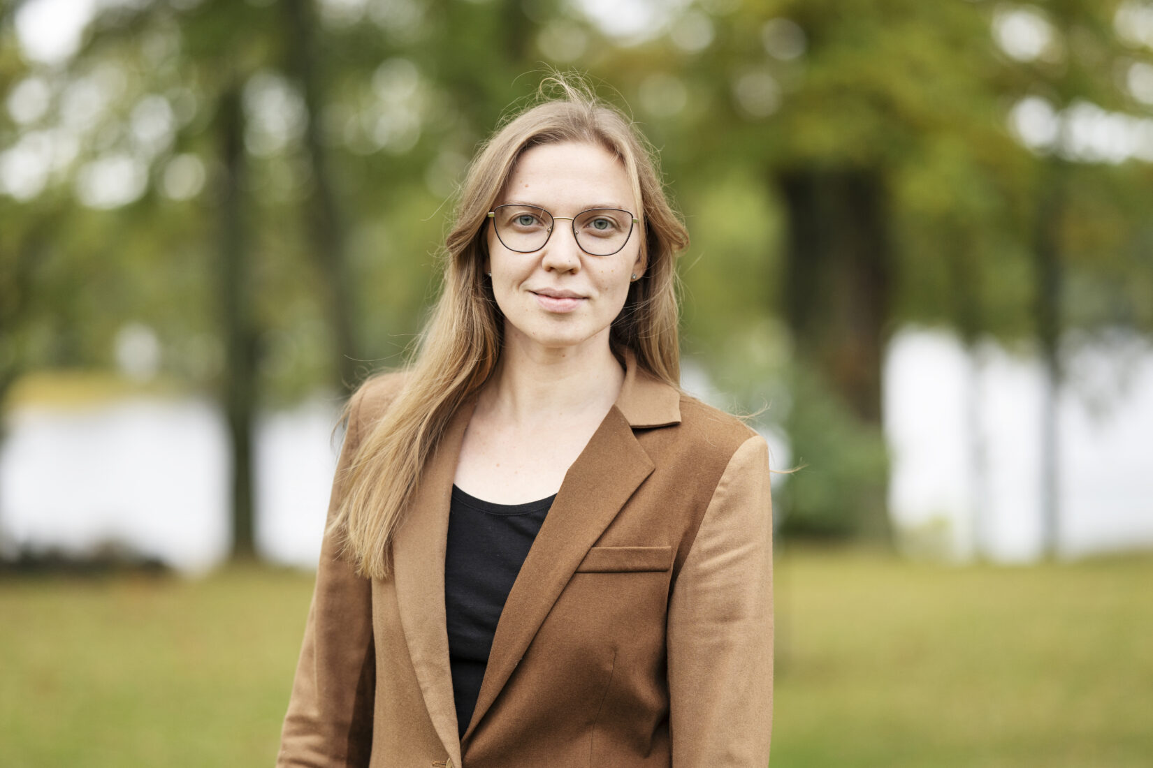 Woman with long hair in brown jacket and glasses.