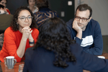 Three participants are sitting around a table having a conversation. 