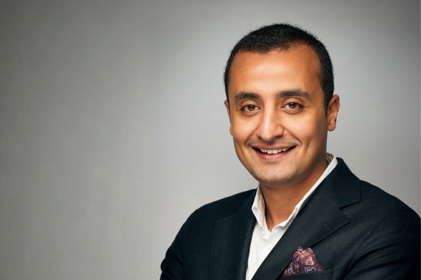 A corporate head shot of a man in a suit smiling at the camera.